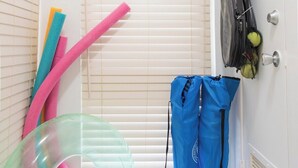 Ein Zimmer mit Tür, einem Fenster mit Jalousien, einem an der Wand befestigten Gepäckträger und einer blauen Tasche.