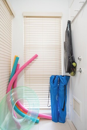 Ein Zimmer mit Tür, einem Fenster mit Jalousien, einem an der Wand befestigten Gepäckträger und einer blauen Tasche.