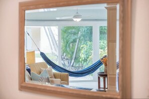 A room with a hammock, a sofa, and a view of palm trees through large windows.