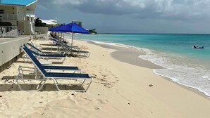 Ein Strand mit Liegestühlen und Sonnenschirmen, ein klarer Himmel und ein ruhiges Meer.