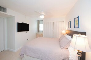 Une chambre à coucher comprenant un lit, un téléviseur fixé au mur, un ventilateur de plafond et une lampe de chevet.