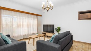 A living room with a sofa, a coffee table, a TV, and a chandelier. - Swainson on Margaret (North Brighton)