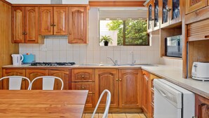 A kitchen with wooden cabinets, a stove, a sink, and a dishwasher. - Swainson on Margaret (North Brighton)
