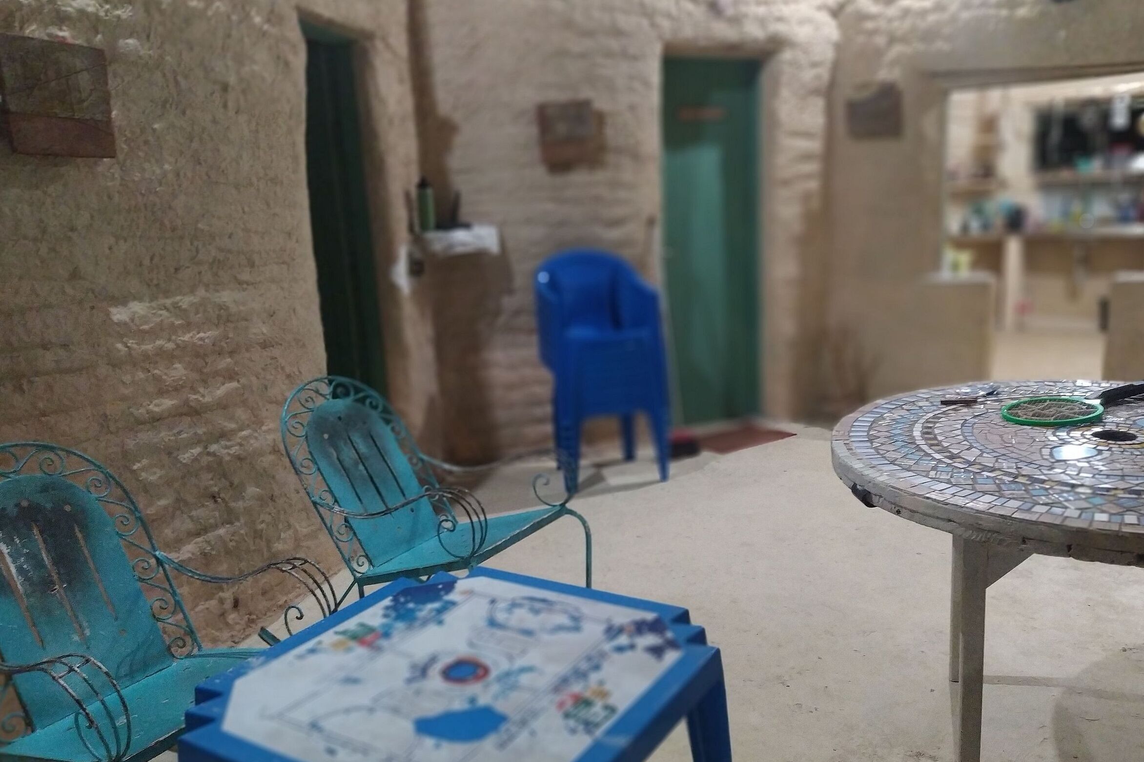 Un pasillo estrecho con una silla de plástico azul y una mesa con cubierta de mosaico.