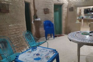 A narrow corridor with a blue plastic chair and a table with a mosaic top. - casa de areia (Aracati)