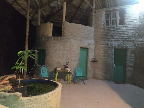 A rustic building with a concrete exterior, a green door, and a small window. There is a table with chairs and a potted plant. - casa de areia (Aracati)