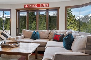 A modern living room with a large window offering a mountain view, a sofa with multiple cushions, and a wooden coffee table.