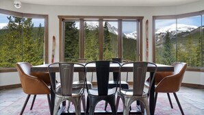 A dining area with a table and chairs, large windows with a mountain view, and a ceiling light fixture.