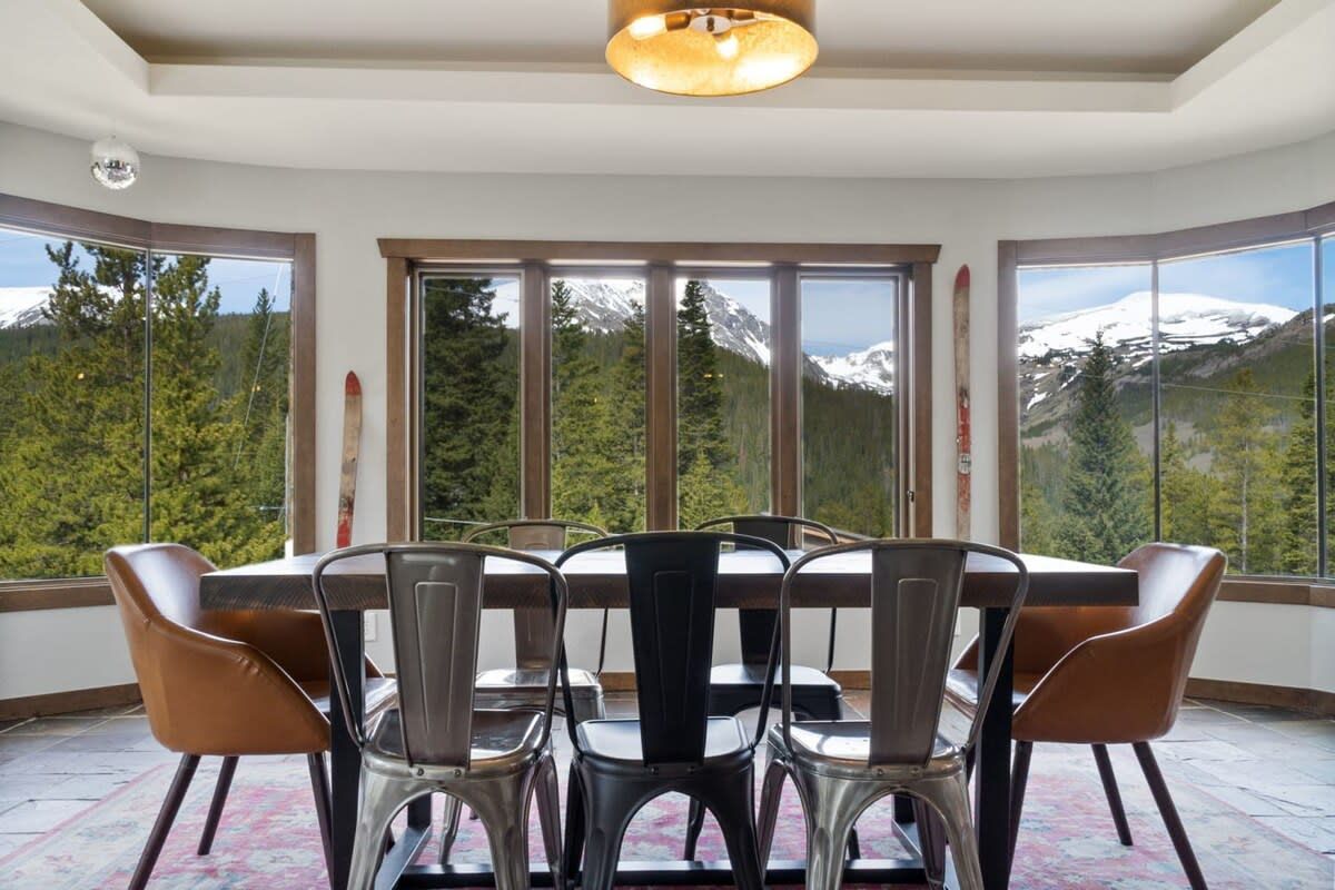 Un espace repas comprenant une table et des chaises, de grandes fenêtres offrant une vue sur les montagnes et un luminaire au plafond.