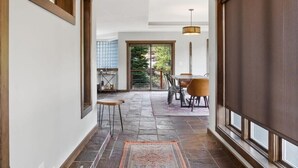 A hallway with stone flooring, a dining area with chairs and a table, and a large window with a view of greenery.