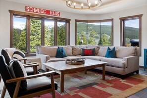 A modern living room with a large sofa, a coffee table, and a view of a mountainous landscape through large windows.