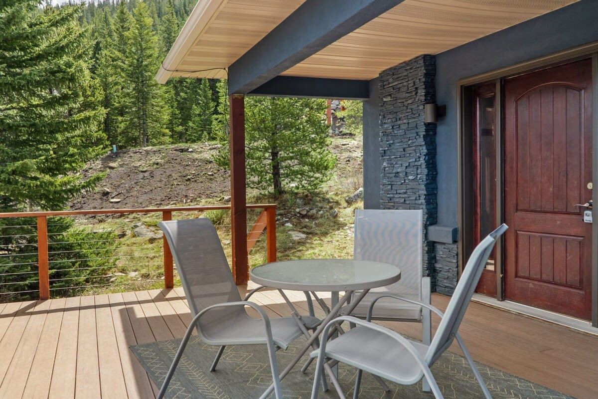 A covered outdoor seating area with a table and chairs, a stone wall, and a wooden door.