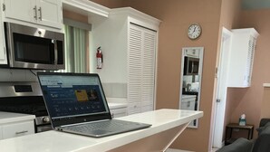 Una cocina con una computadora portátil sobre una encimera blanca, un taburete negro y un reloj en la pared.
