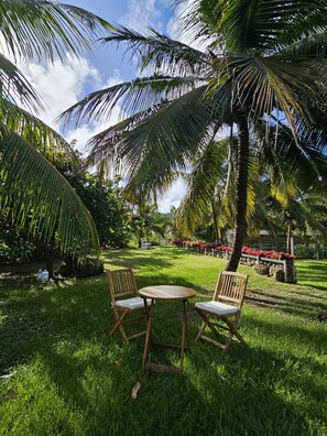 Un jardin tropical avec une table et des chaises en bois, des palmiers et un ciel dégagé.