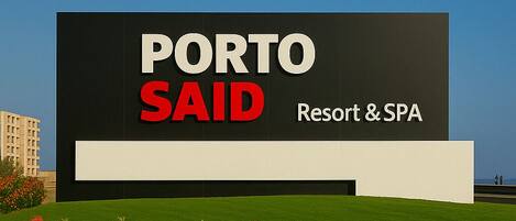 A sign for Porto Said Resort & SPA with a modern design and a landscaped garden in the foreground.