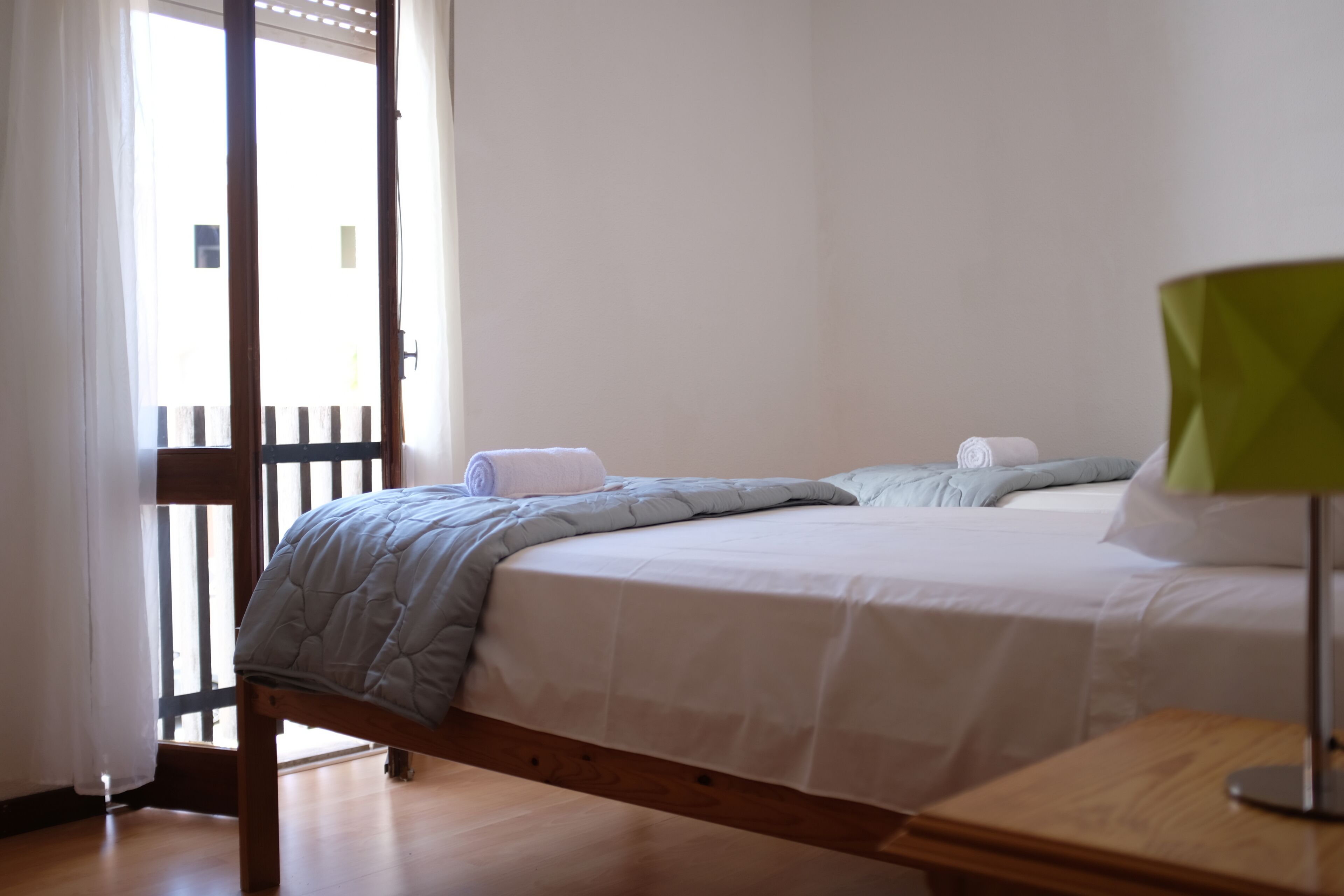 Un dormitorio con una cama, una mesita de noche de madera, una lámpara verde y una ventana con cortinas.
