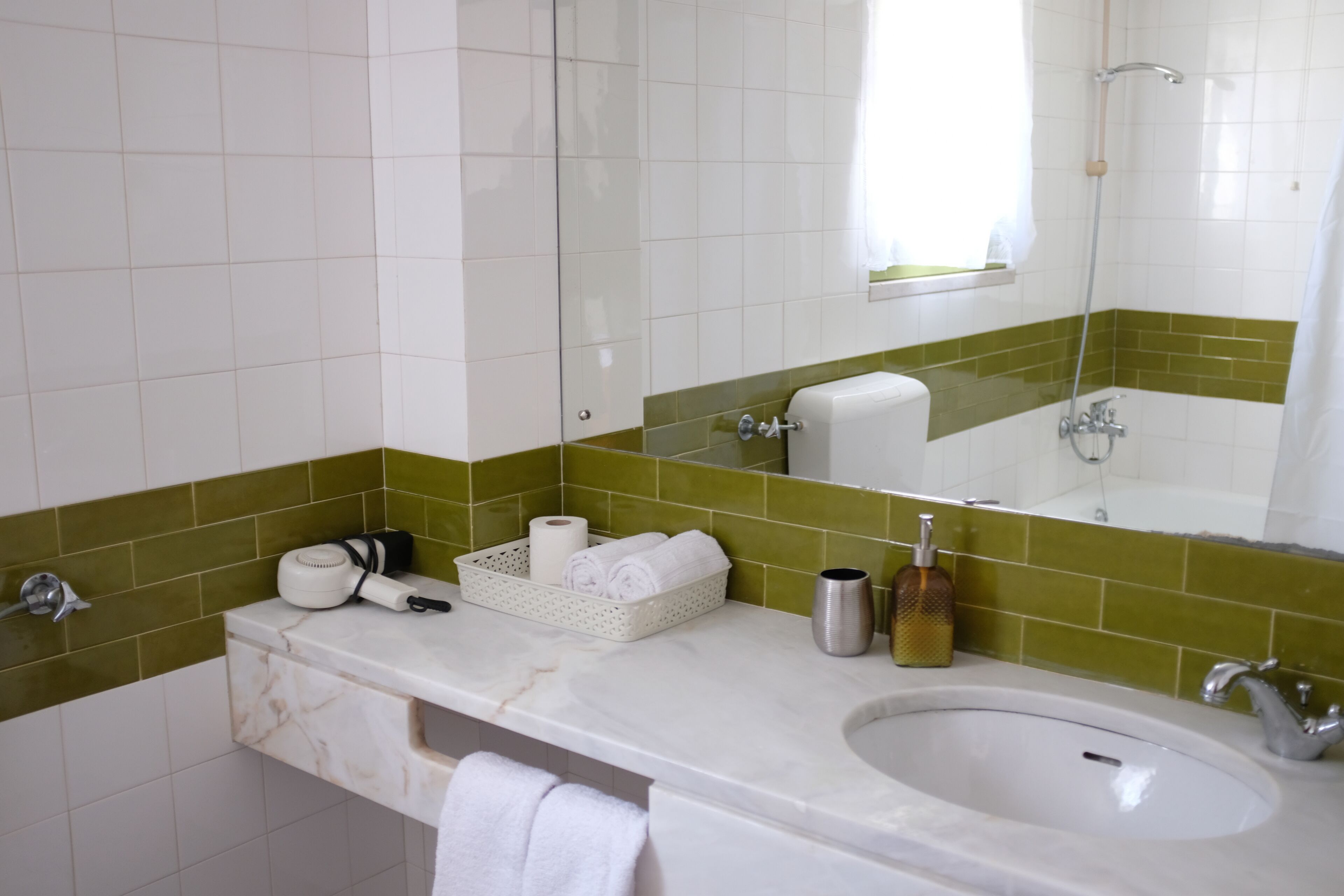 A bathroom with a white sink, green-tiled walls, a mirror, and a shower.