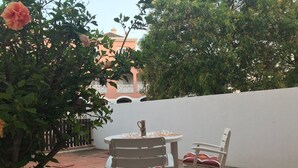 An outdoor patio with a table and two chairs, surrounded by greenery and a white wall. - Marina Gardens, Relaxing Duplex in Central Location (Quarteira)