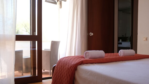 A hotel room with a bed, a chair, and a view through a glass door. - Marina Gardens, Relaxing Duplex in Central Location (Quarteira)