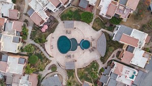 An aerial view of a residential area with a central swimming pool, surrounded by houses with red-tiled roofs. - Private Villa in Gated Community  (Cabo San Lucas)