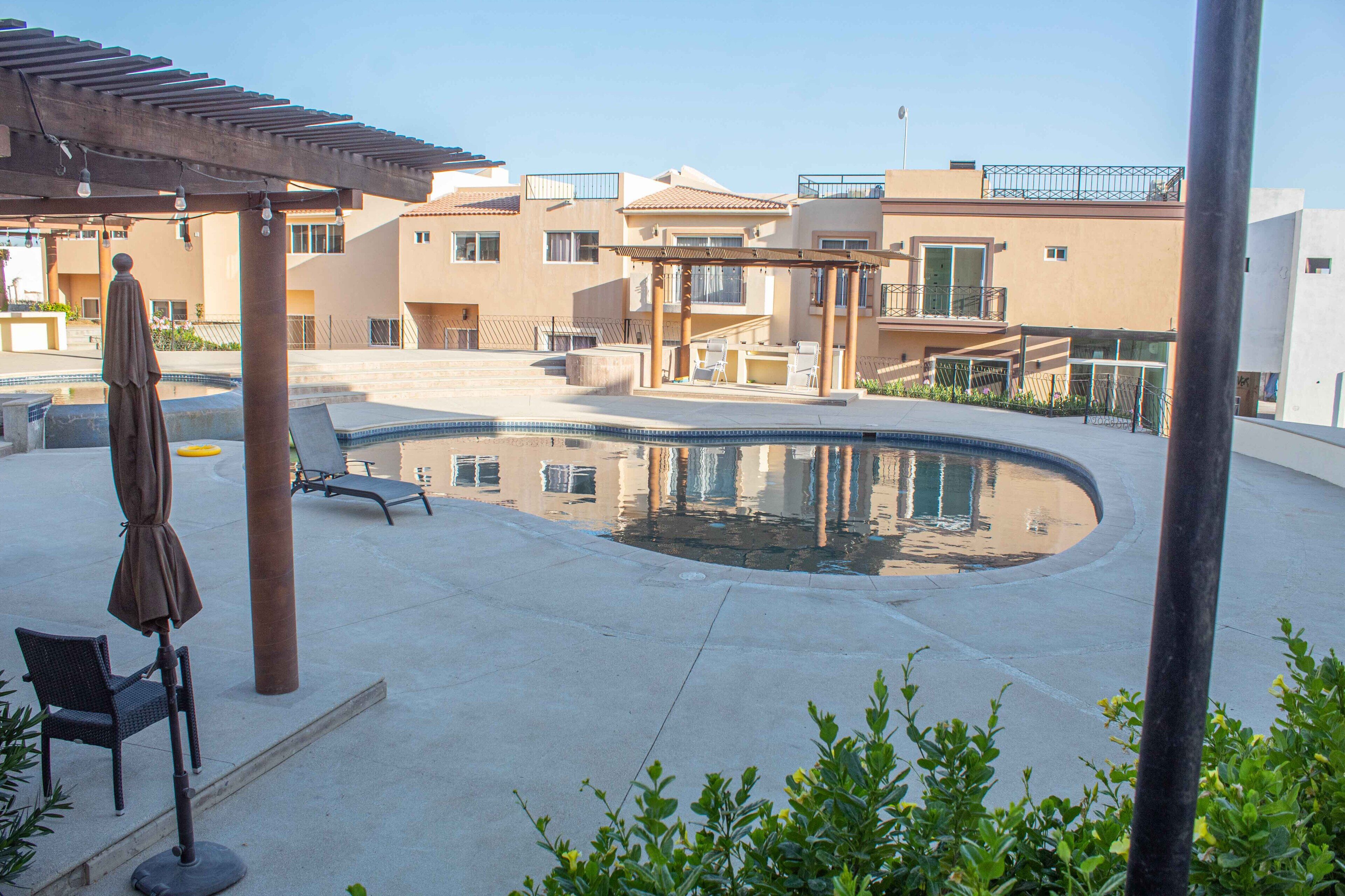 A pool area with a pergola, lounge chairs, and a small table.