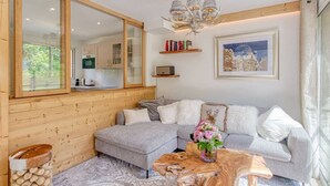 A modern living room with a large mirror, a wooden ceiling, a chandelier, a grey sofa, and a wooden coffee table.