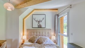 A bedroom with a large bed, two bedside lamps, a framed deer picture, and a window with curtains.