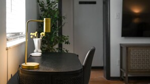 Una mesa de comedor con tablero negro, una lámpara dorada y un florero blanco con flores amarillas.