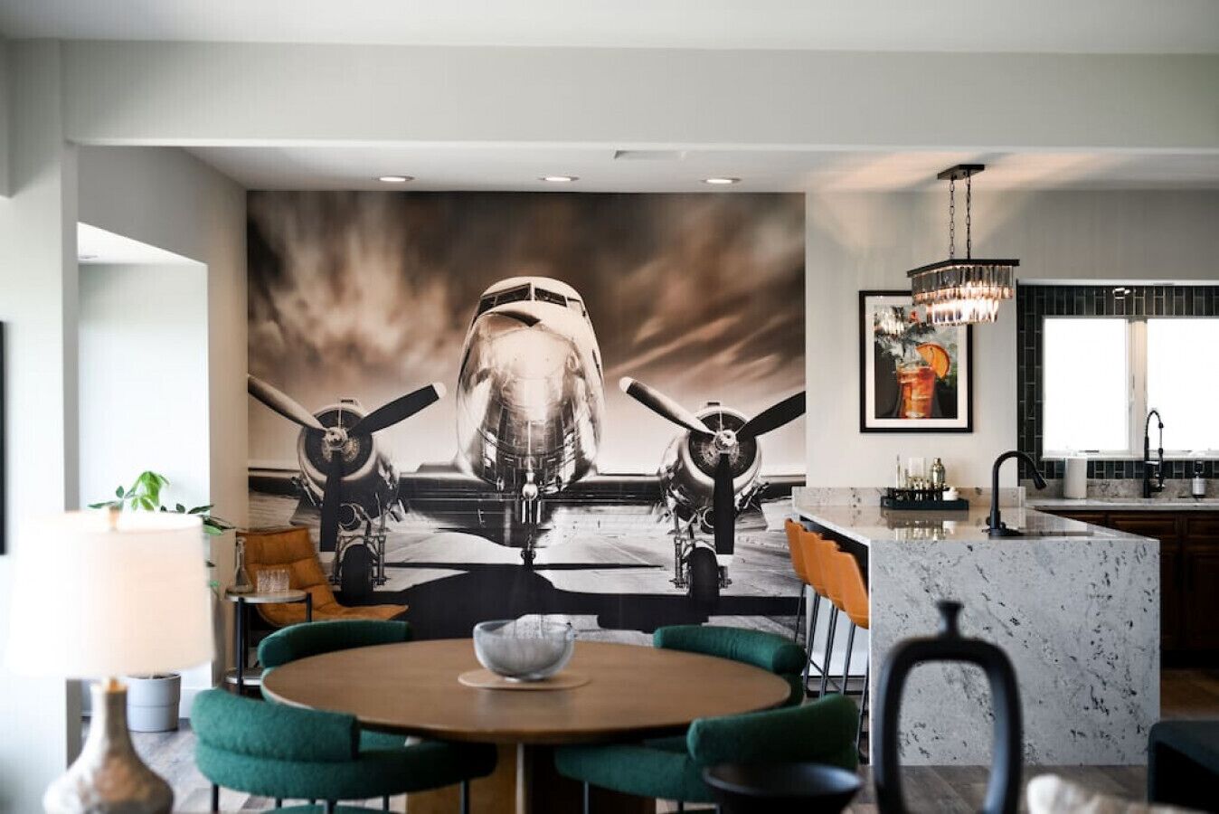 A modern kitchen with a large mural of a vintage aircraft, a round dining table with chairs, and a bar area with a chandelier.