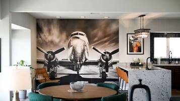A modern kitchen with a large mural of a vintage aircraft, a round dining table with chairs, and a bar area with a chandelier.