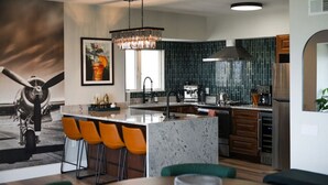 Una cocina moderna con una isla central, taburetes de bar, una lámpara colgante y un amplio ventanal.