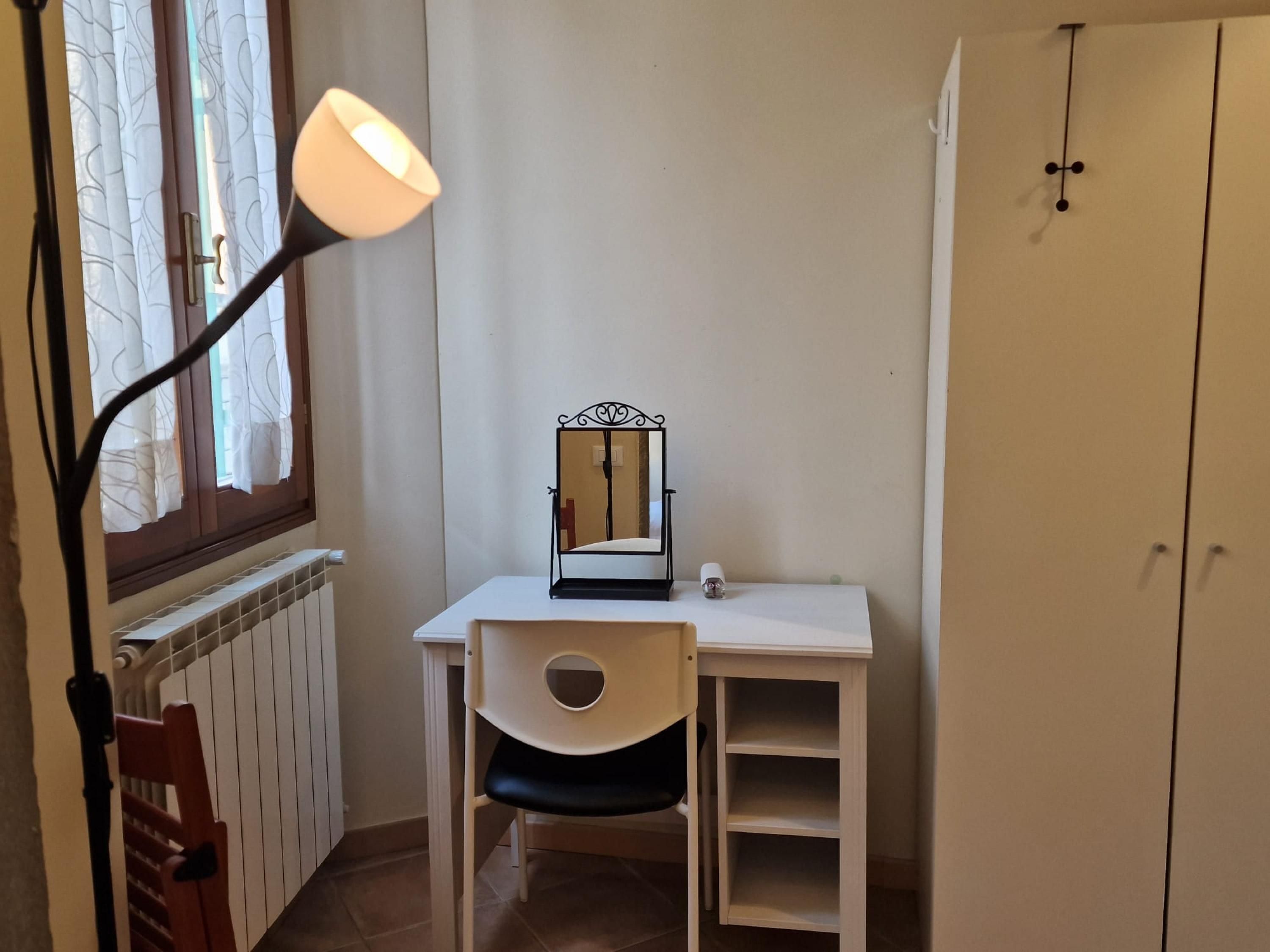 Une pièce comprenant un bureau, une chaise, un miroir, une lampe, un radiateur et une armoire.