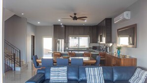 A modern living room with a blue leather sofa, a dining area with wooden furniture, and a kitchen with dark cabinets and a ceiling fan. - Private Villa in Gated Community (Cabo San Lucas)