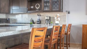 A kitchen with dark wooden cabinets, a granite countertop, a coffee maker, and four wooden chairs. - Private Villa in Gated Community (Cabo San Lucas)