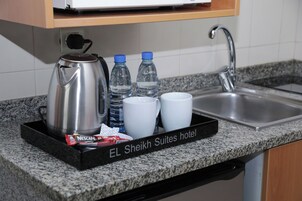 Eine Küchenzeile mit Kaffeemaschine, Wasserflaschen und Tassen, sowie ein Schild mit dem Hotelnamen.