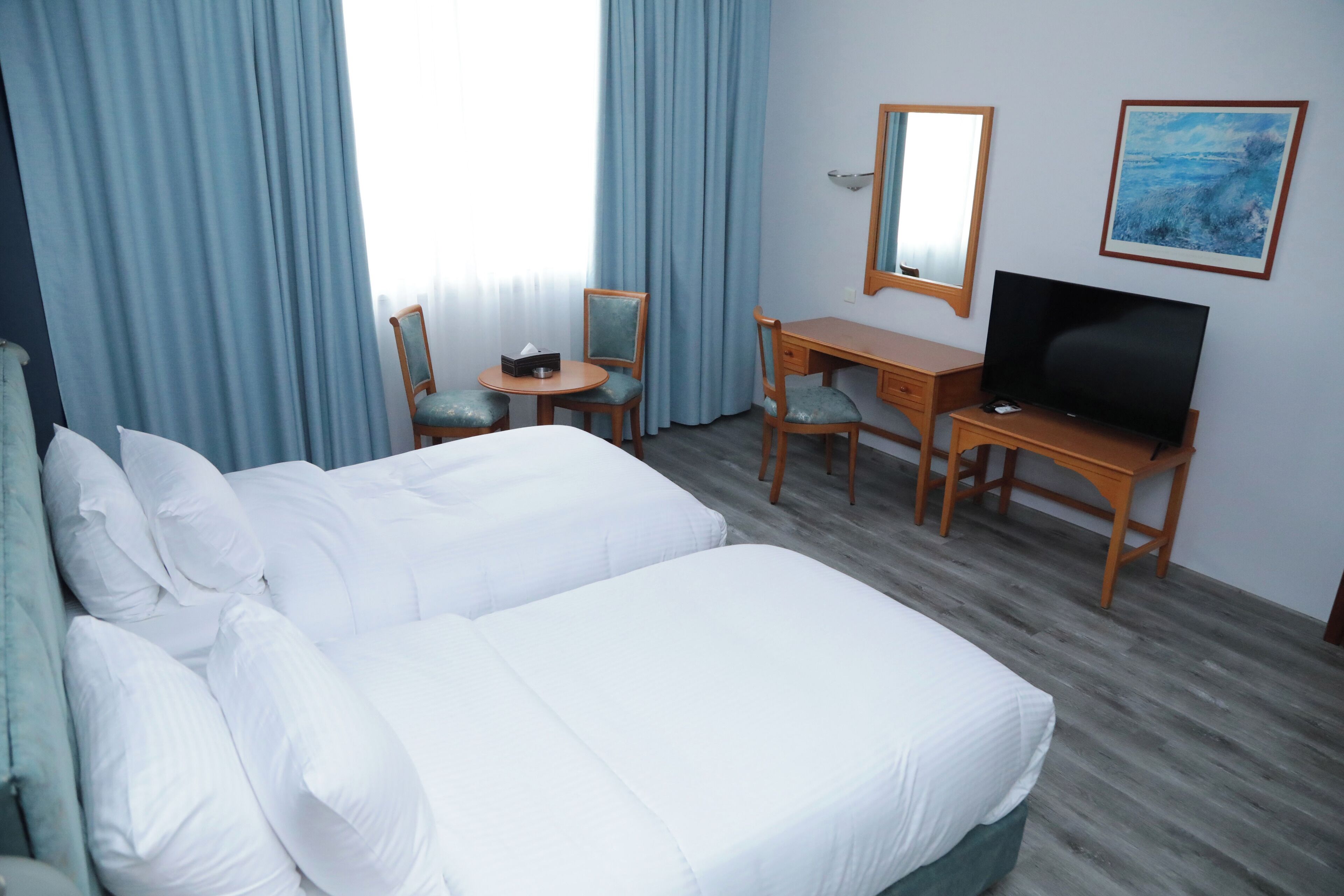 Habitación de hotel con una cama grande, un escritorio, una silla, un televisor y un cuadro en la pared.
