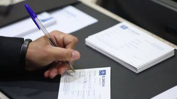 Una persona firmando un documento en un escritorio con un bolígrafo.