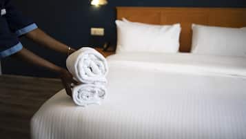Un lit bien fait, avec du linge de lit blanc et des oreillers, une tête de lit en bois et un luminaire fixé au mur.