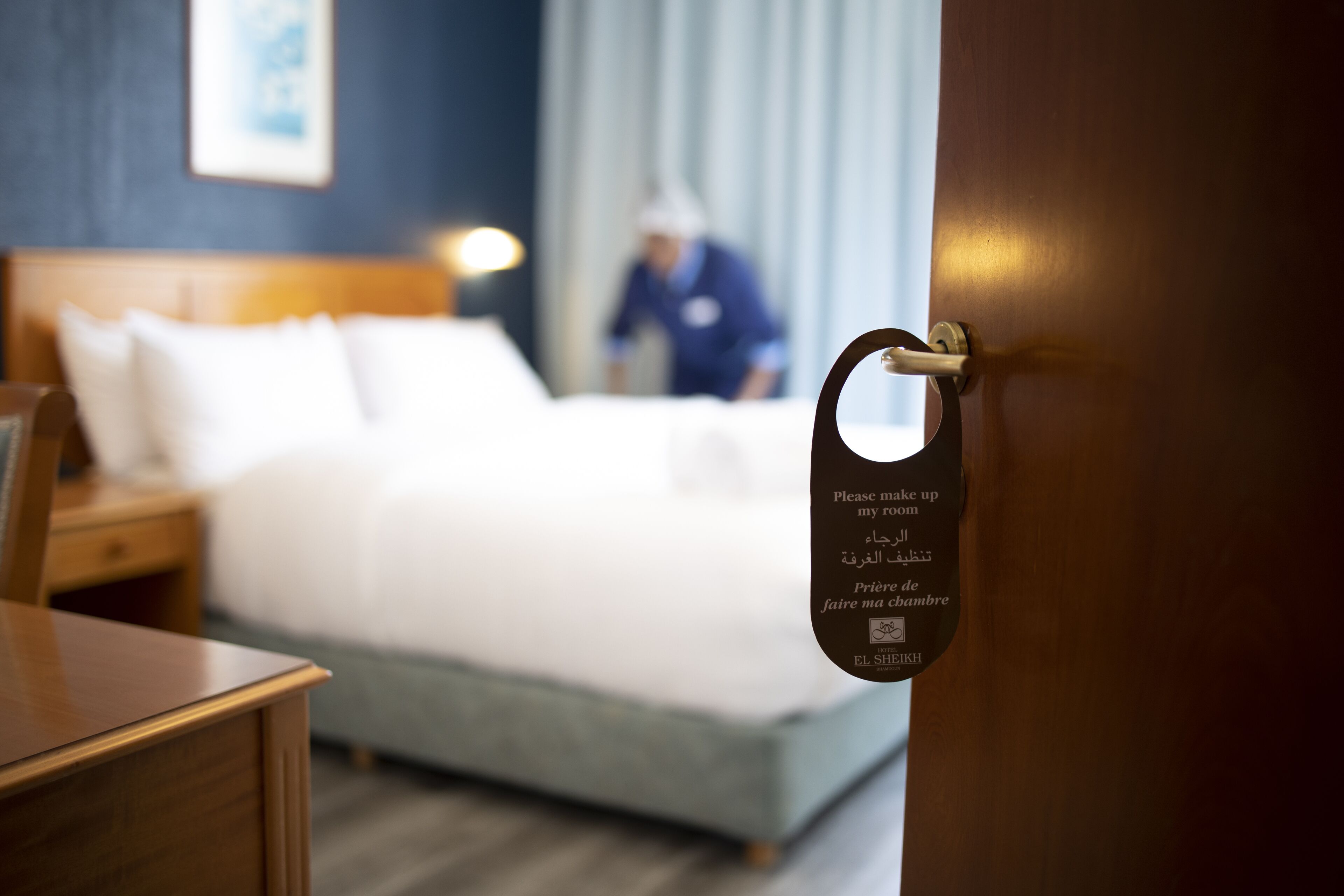 Une chambre d’hôtel avec un lit, une table de chevet et une porte sur laquelle est apposée une pancarte rédigée en plusieurs langues.