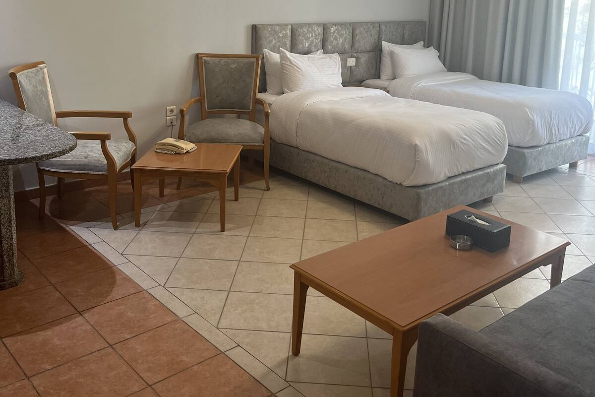 A hotel room with a bed, two chairs, a small table, a sofa, and a window with curtains.