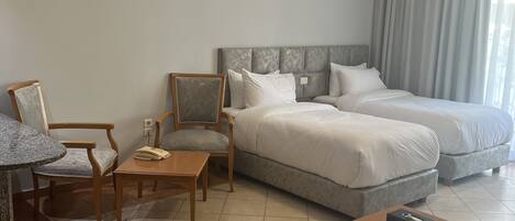 A hotel room with a bed, two chairs, a small table, a sofa, and a window with curtains.