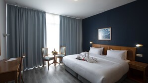 A hotel room with a large bed, a desk, a chair, and a small table with a vase and picture frame. - El Sheikh Suites Hotel (Beirut)
