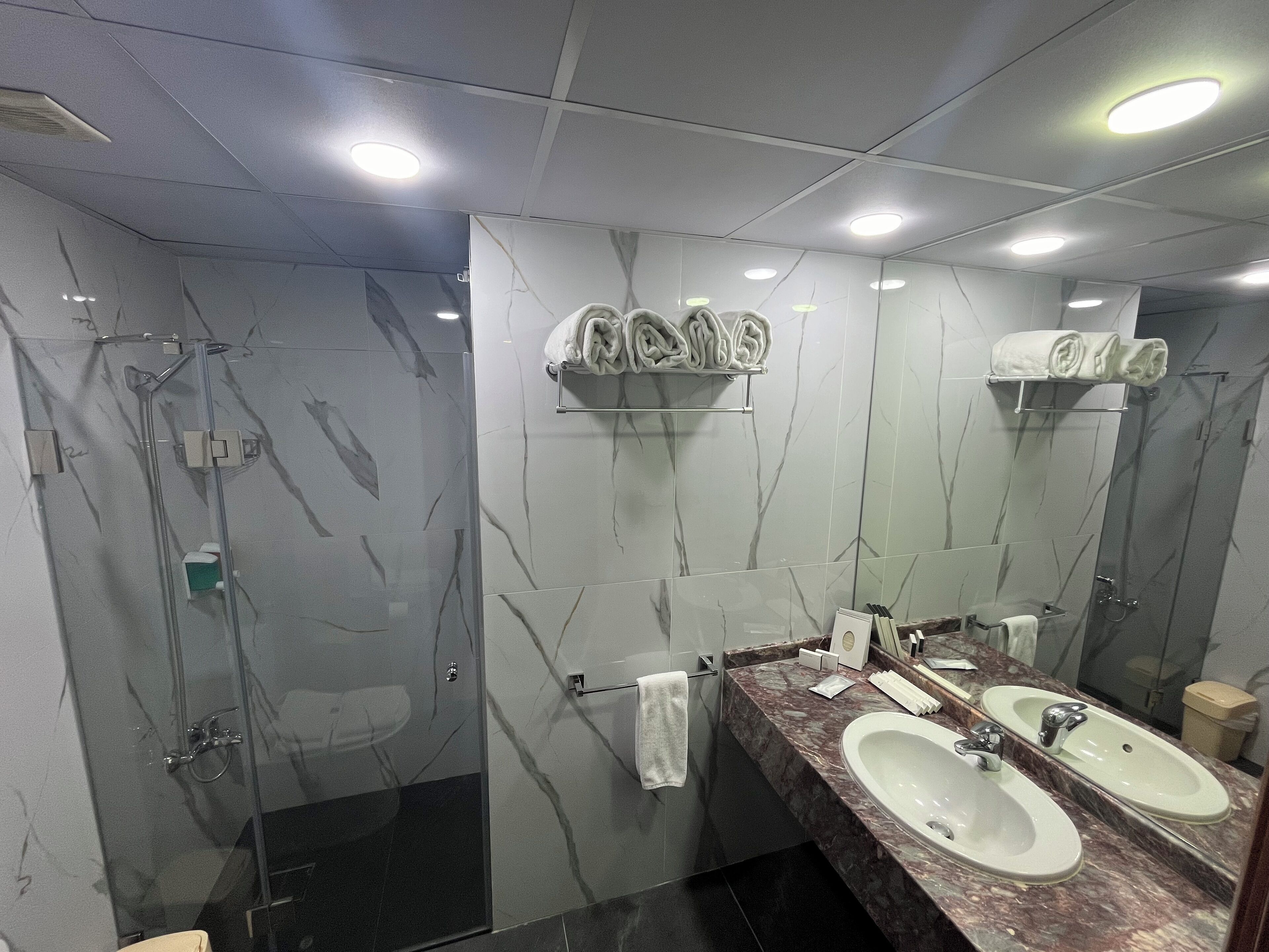 Une salle de bain moderne dotée d’une douche à parois de verre, de murs en marbre et de deux vasques avec des miroirs.