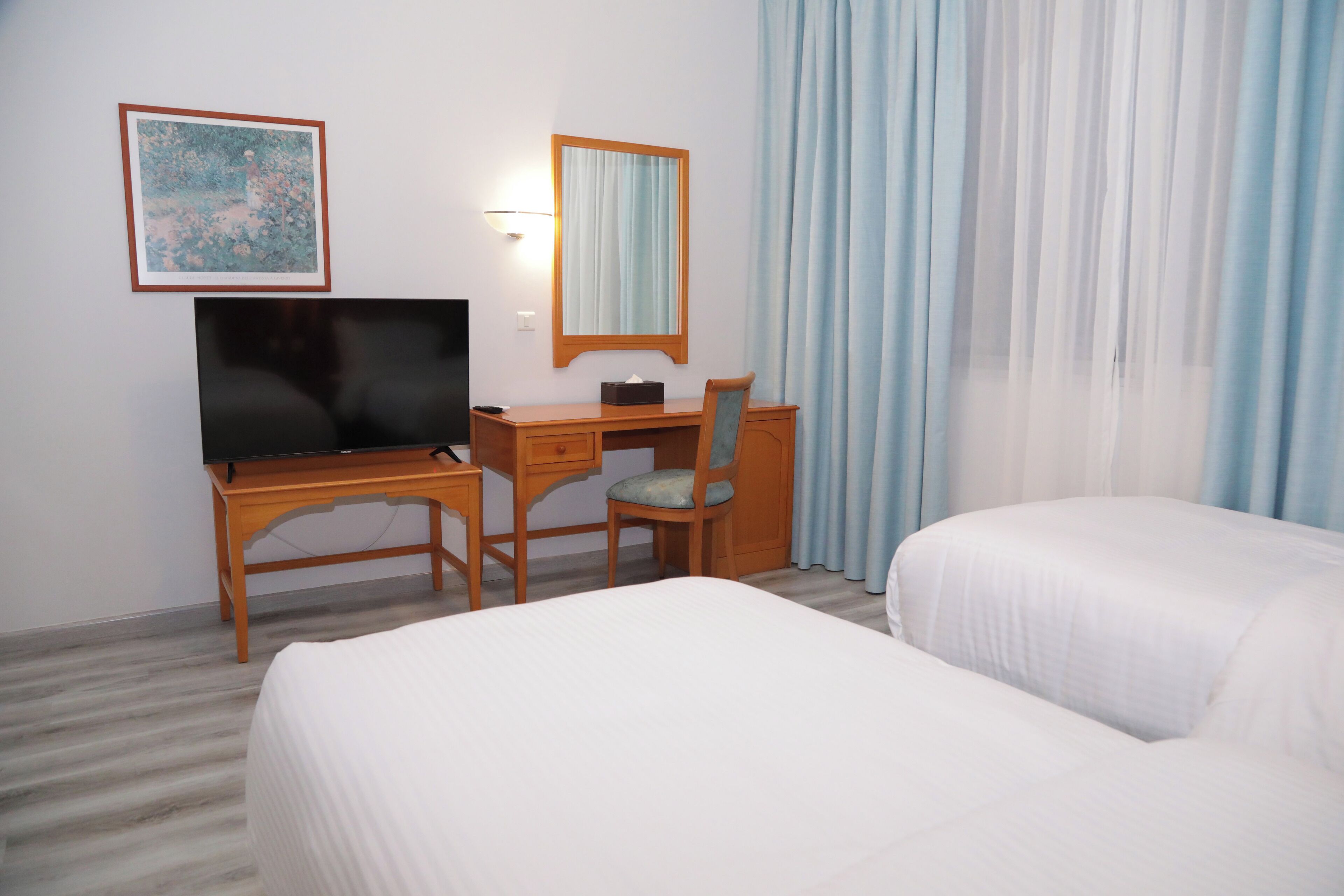 Ein Hotelzimmer mit Bett, Schreibtisch mit Computer, Stuhl, Fernseher, Spiegel und einem Fenster mit Vorhängen.
