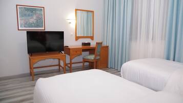 Ein Hotelzimmer mit Bett, Schreibtisch mit Computer, Stuhl, Fernseher, Spiegel und einem Fenster mit Vorhängen.