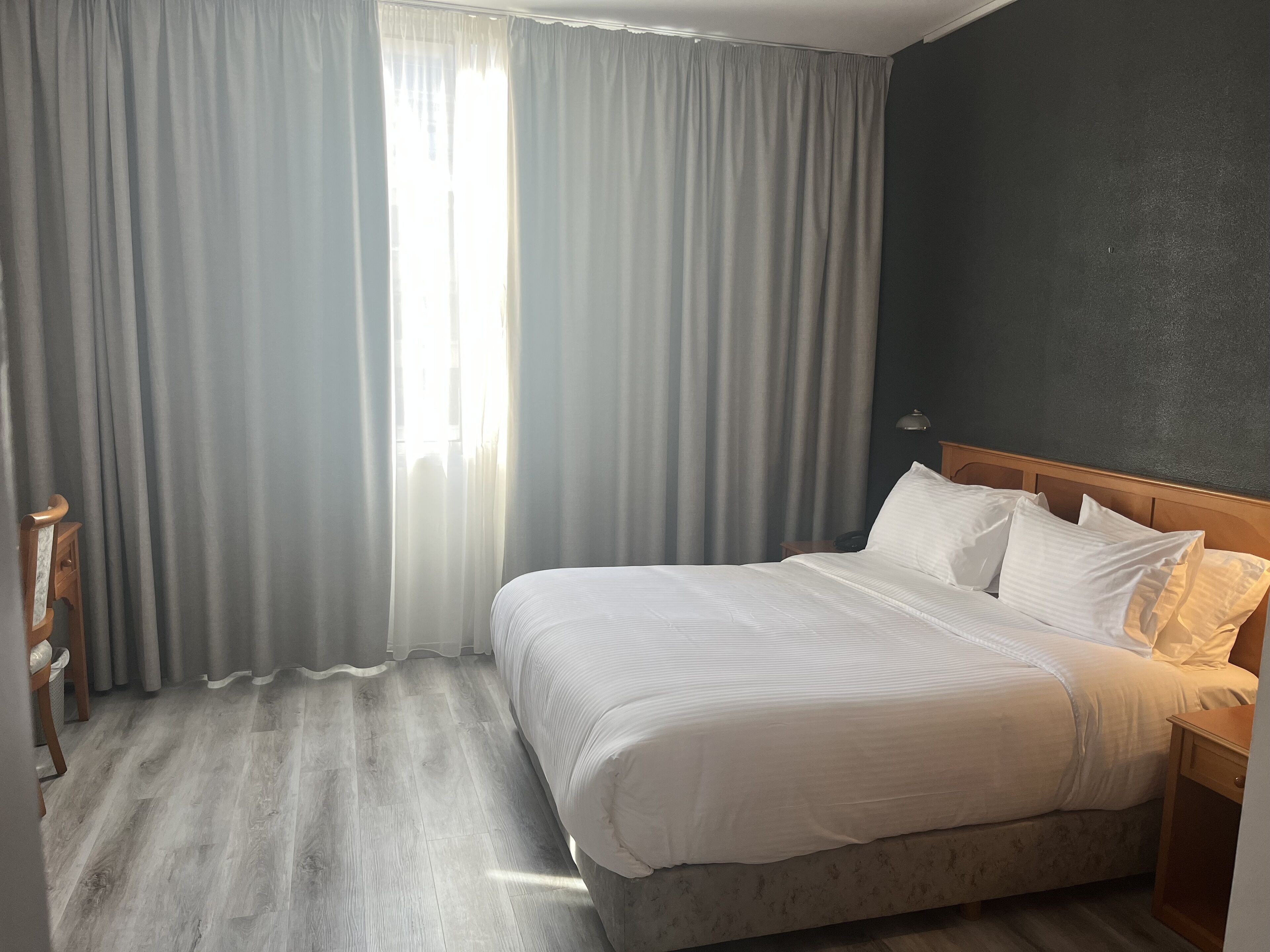 A hotel room with a large bed, grey curtains, and a wooden headboard.