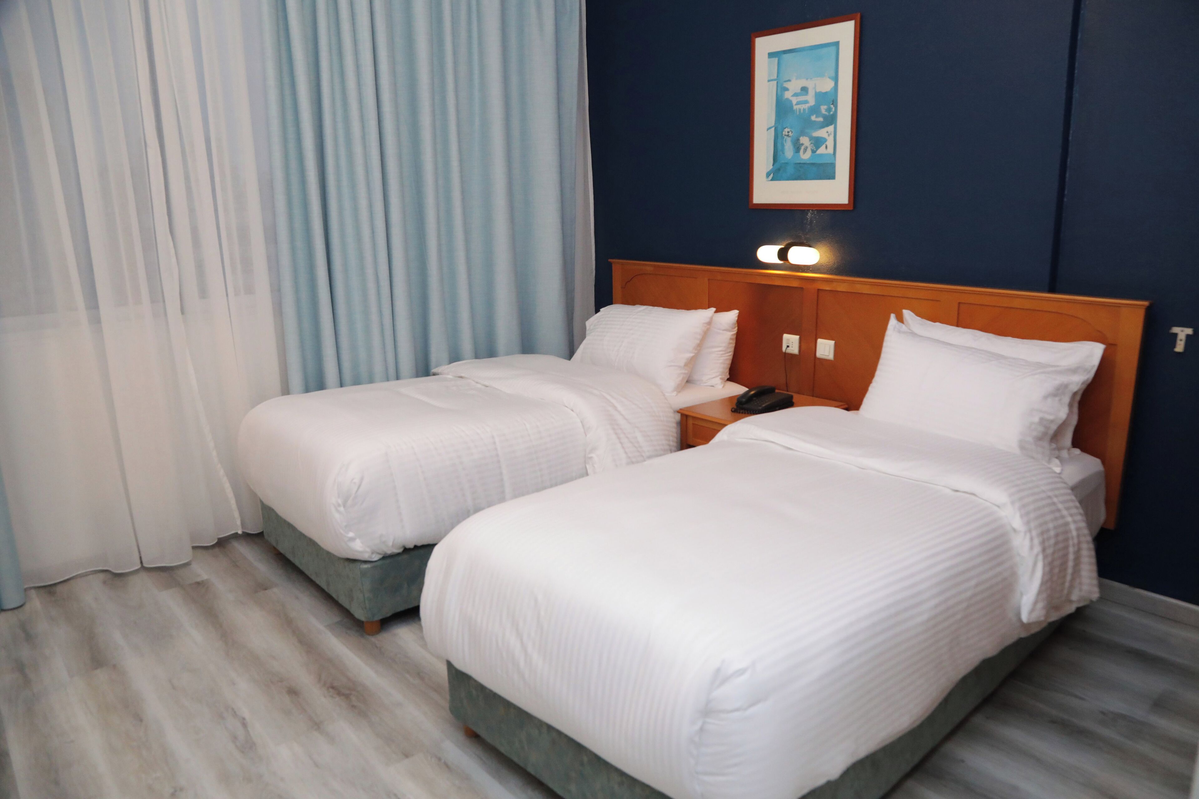 A hotel room with two beds, a wooden headboard, a nightstand, and a painting on the wall.