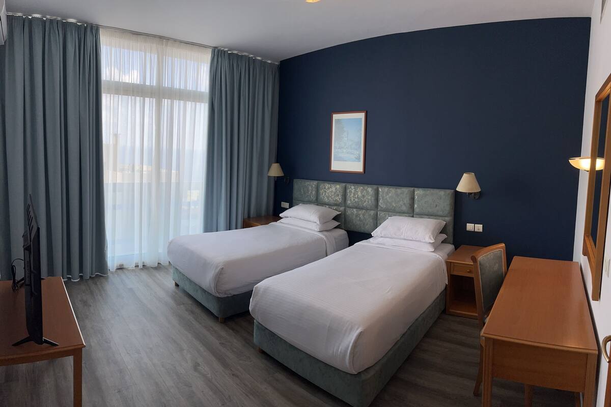 A hotel room with two beds, a desk, a chair, a TV, and a window with curtains.