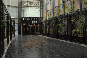 The entrance of Al Sheikh Hotel with a tiled floor and a sign above the entrance.
