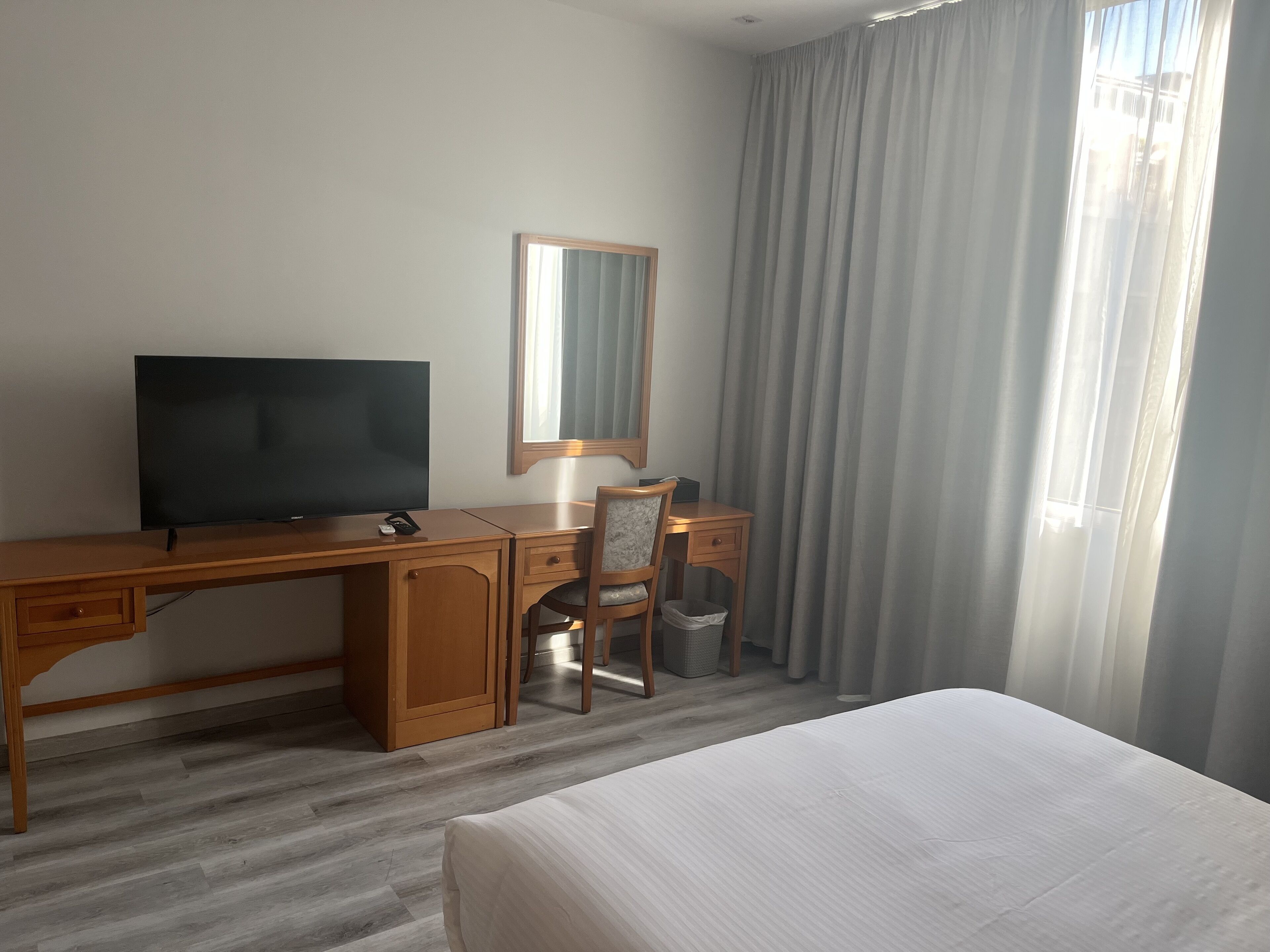 Habitación de hotel con un escritorio de madera, televisor, silla, cama y ventana con cortinas.